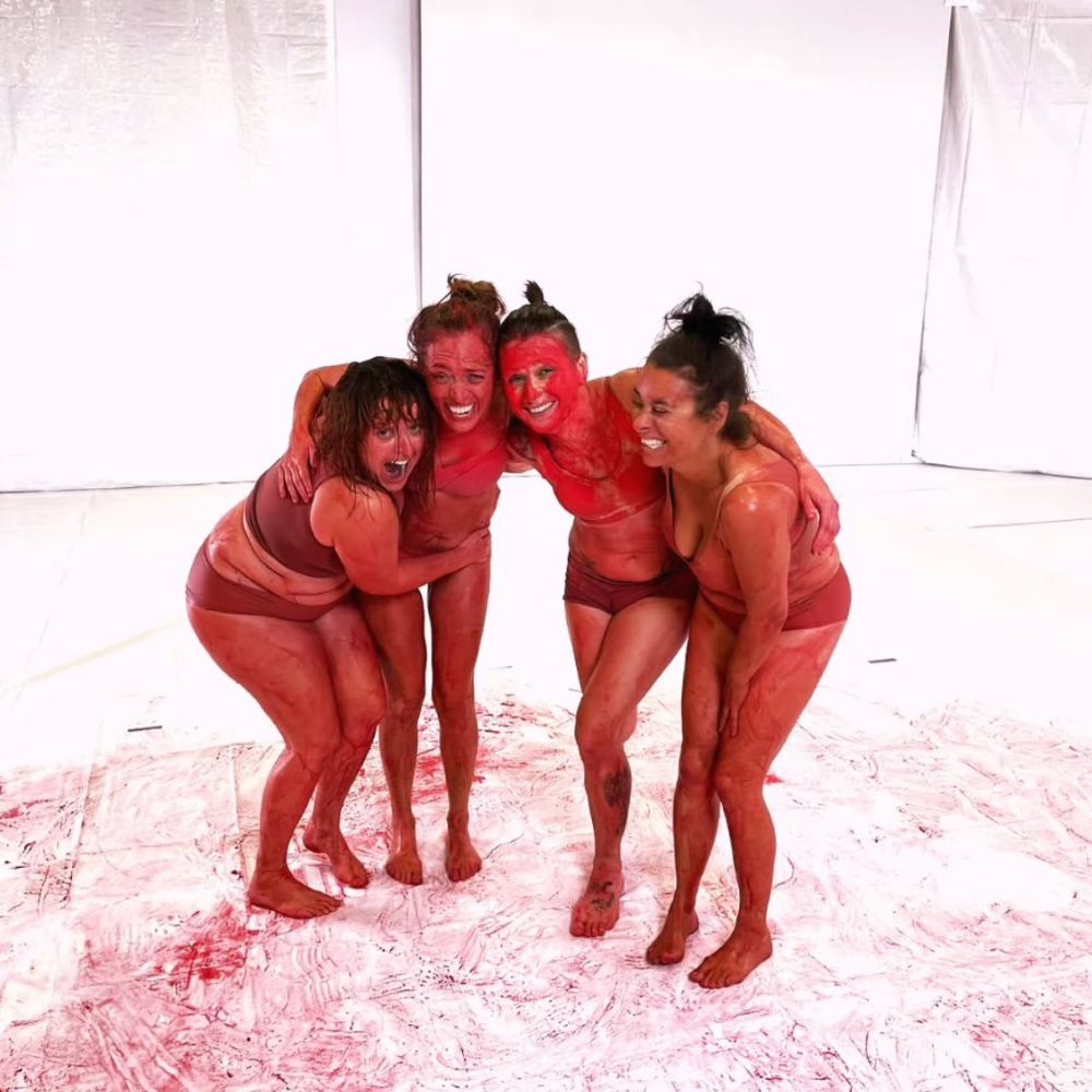 Das abschließende Foto vom Musikvideodreh. 4 Mädels voller roter Farbe lächeln in die Kamera.